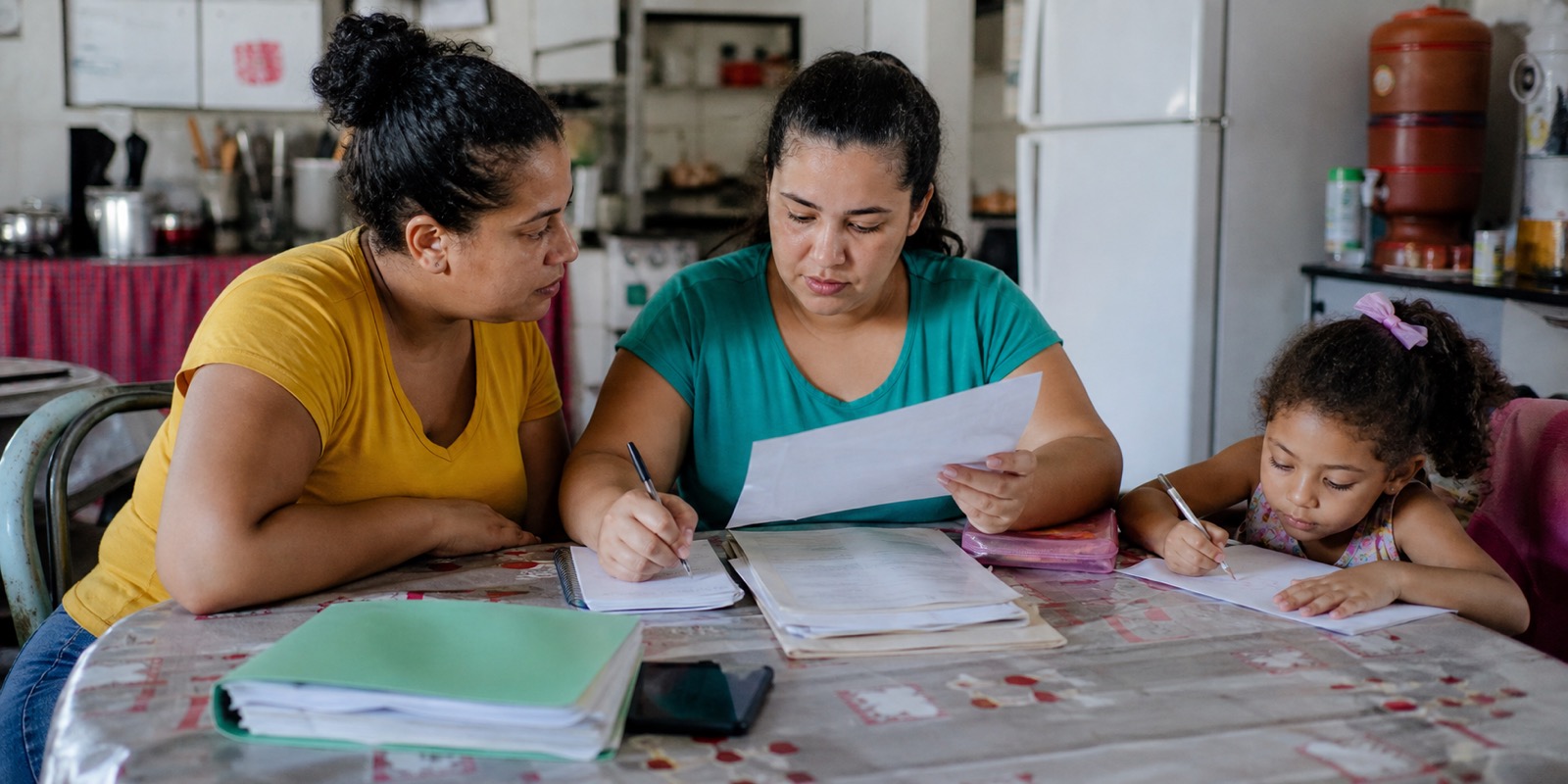 Mãe organiza documentos de saúde com apoio familiar enquanto a criança desenha ao lado.